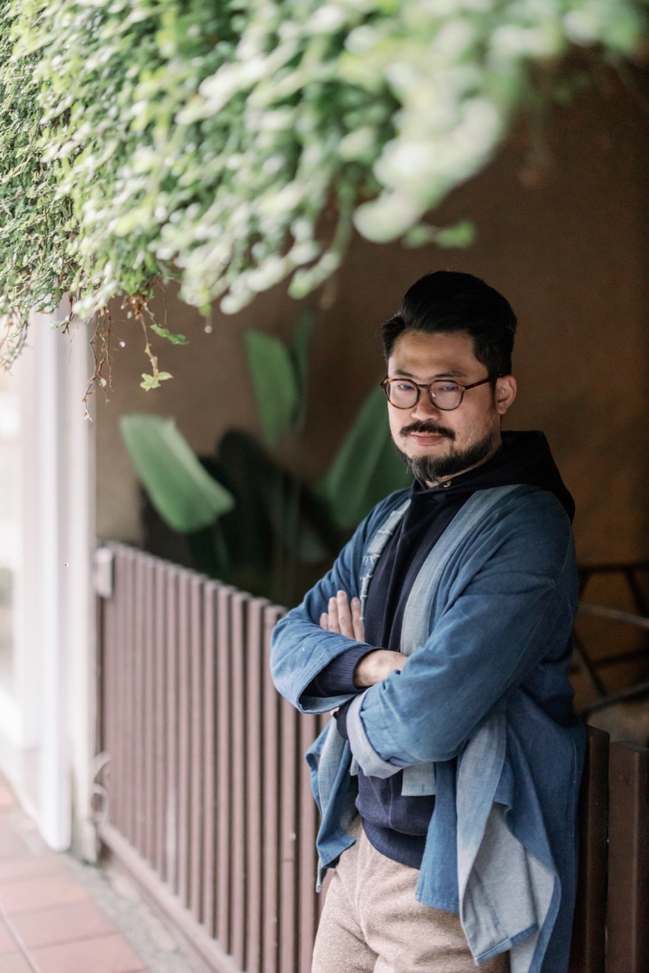 鬍丘 LEO 在室內窗邊，穿著藍色外套站立。