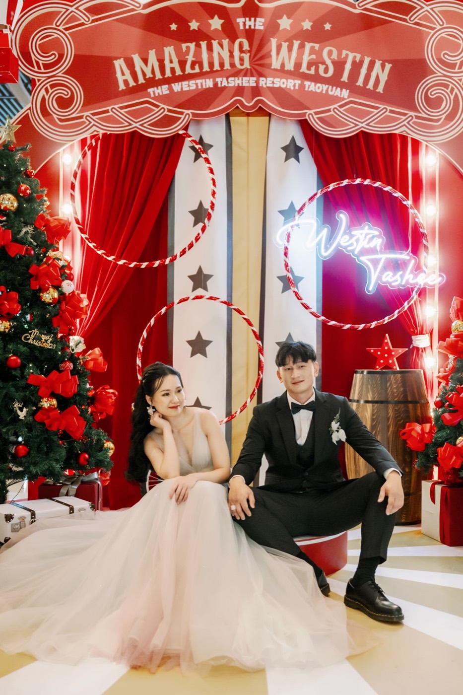 KAI 與 KARA 在紅色馬戲團風格婚禮場景前合照。